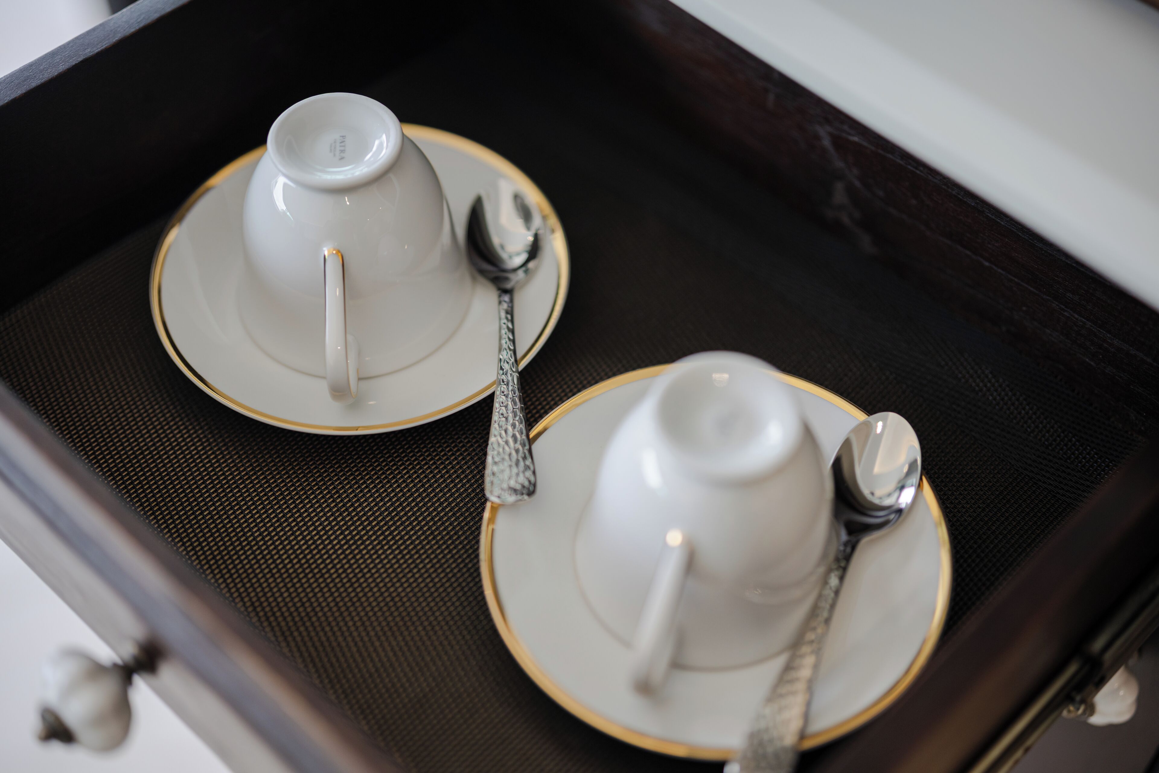 A close-up of a tray with two white teacups and spoons, placed on a textured surface.