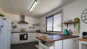 Et moderne køkken med hvide skabe, en træbordplade, indbygget ovn, vask og et vindue med persienner.