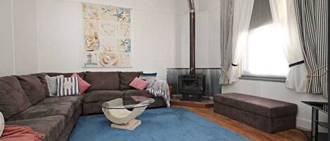 A cozy living room with a sectional sofa, a blue rug, a fireplace, and a decorative wall piece.