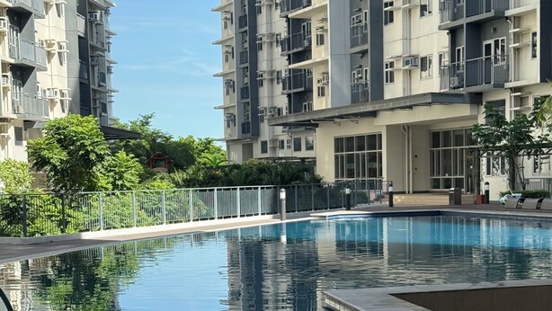 Un moderno edificio residencial con piscina, rodeado de vegetación y un cielo despejado.