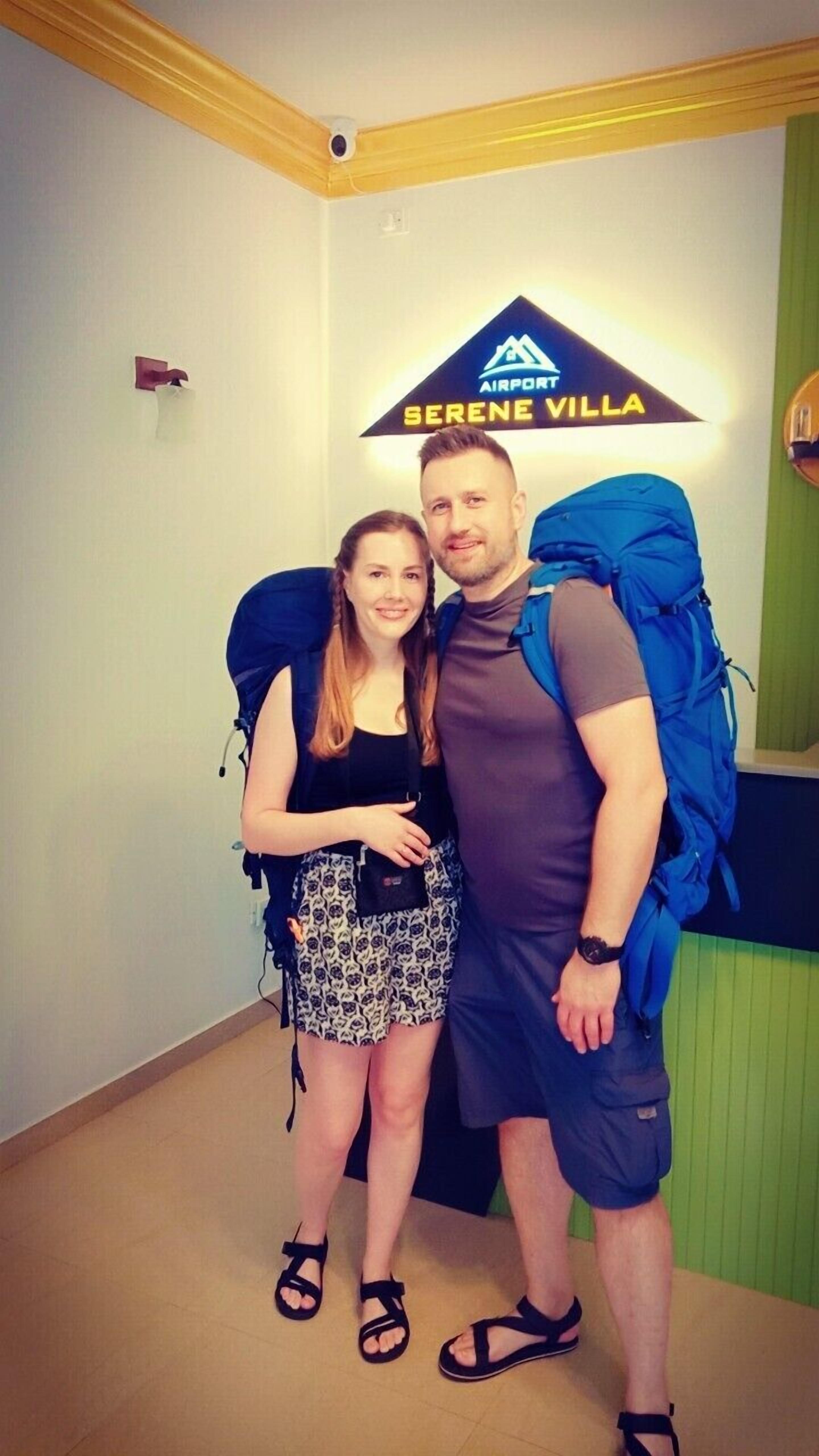 Una habitación con un cartel que dice "SERENE VILLA" y una mochila azul grande en el suelo.