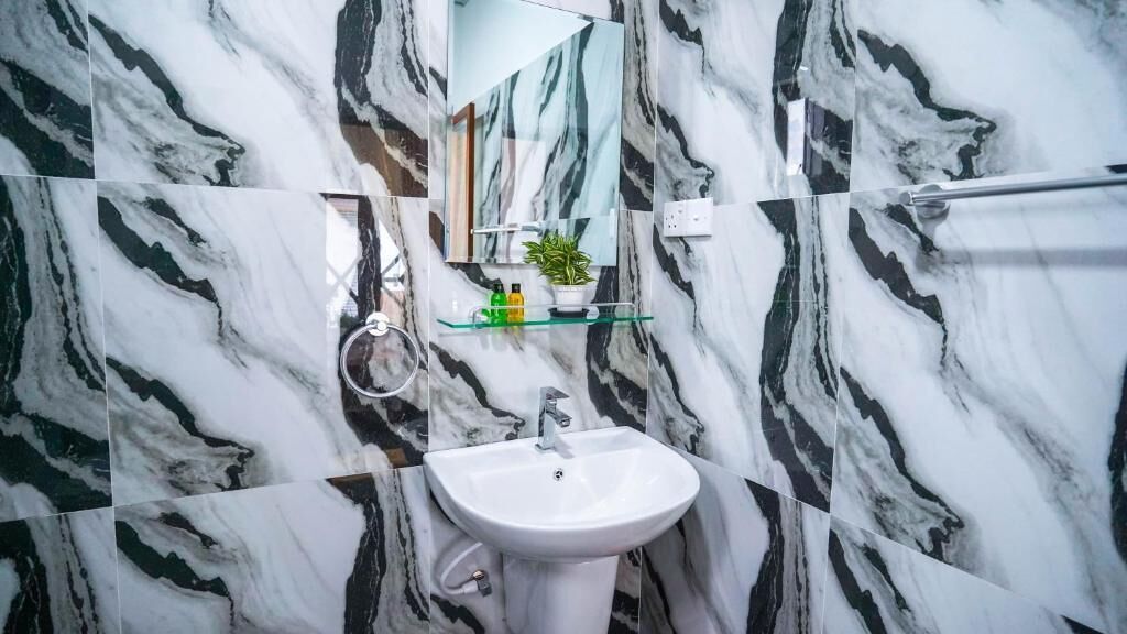 Une salle de bain avec un lavabo blanc, une étagère en verre où sont rangés les articles de toilette, et un miroir au-dessus du lavabo.