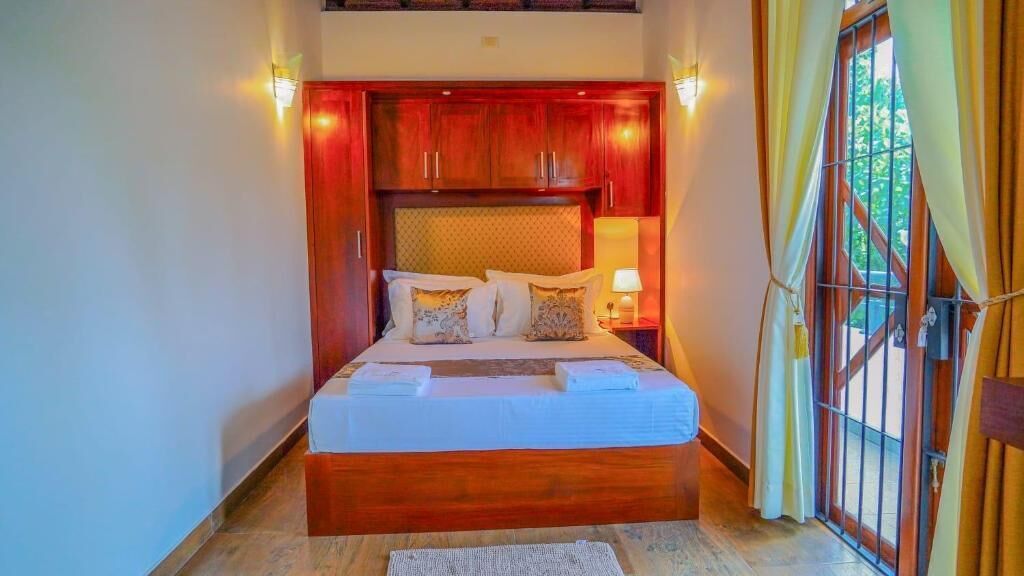 A bedroom with a wooden headboard, a bed with pillows, a nightstand, and a window with curtains.