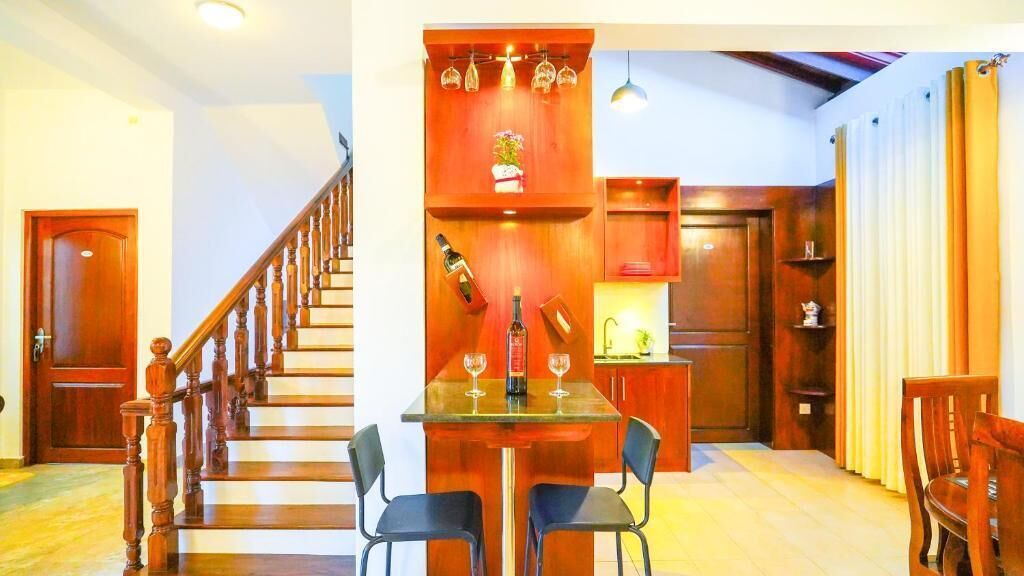 Una cocina con una escalera de madera, una mesa de comedor con sillas y una estantería empotrada para vinos.