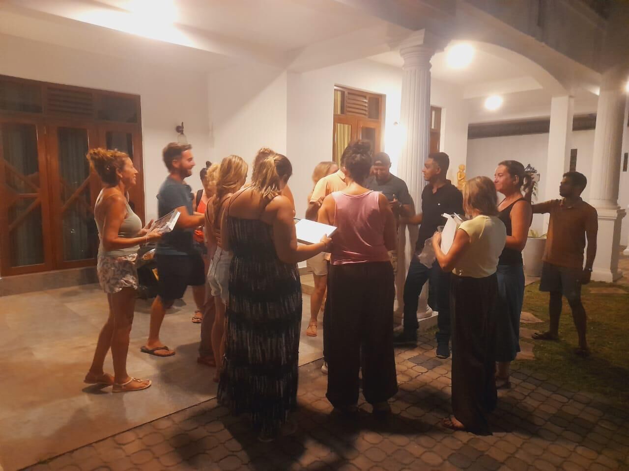 Un grupo de personas reunidas en un espacio al aire libre con suelo de baldosas y paredes blancas.