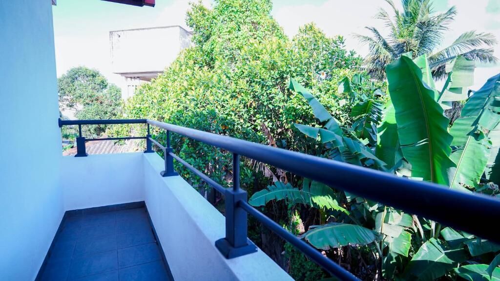 A balcony with a metal railing overlooking lush greenery and a building in the background.