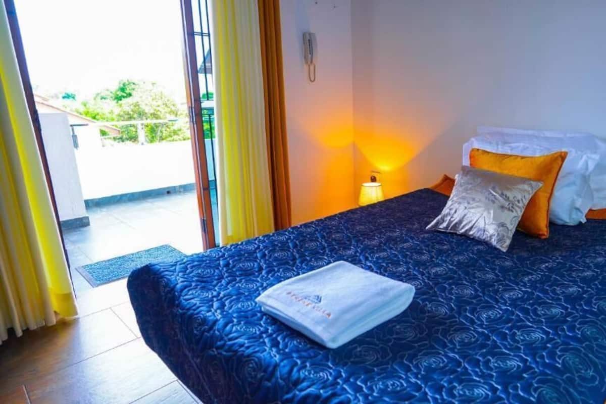 Ein Hotelzimmer mit Bett, Nachttisch, Lampe und Blick ins Freie.