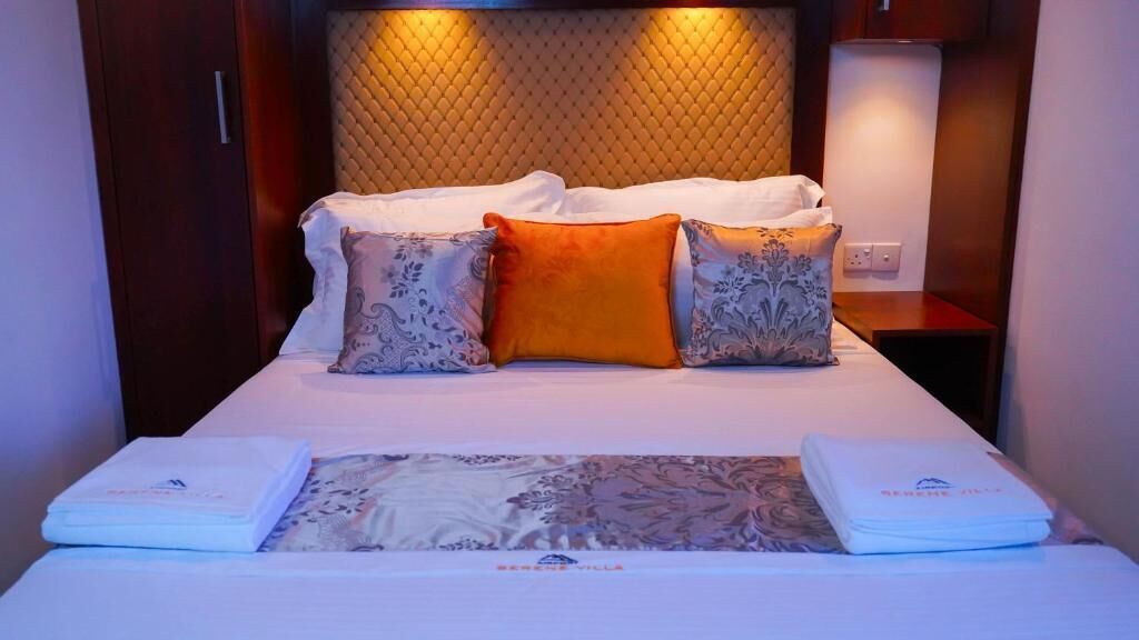 A neatly made bed with a patterned bedspread, two pillows, and folded towels on either side.