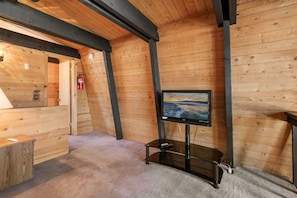 A cozy wooden room with a television on a stand, a fire extinguisher, and a small desk.