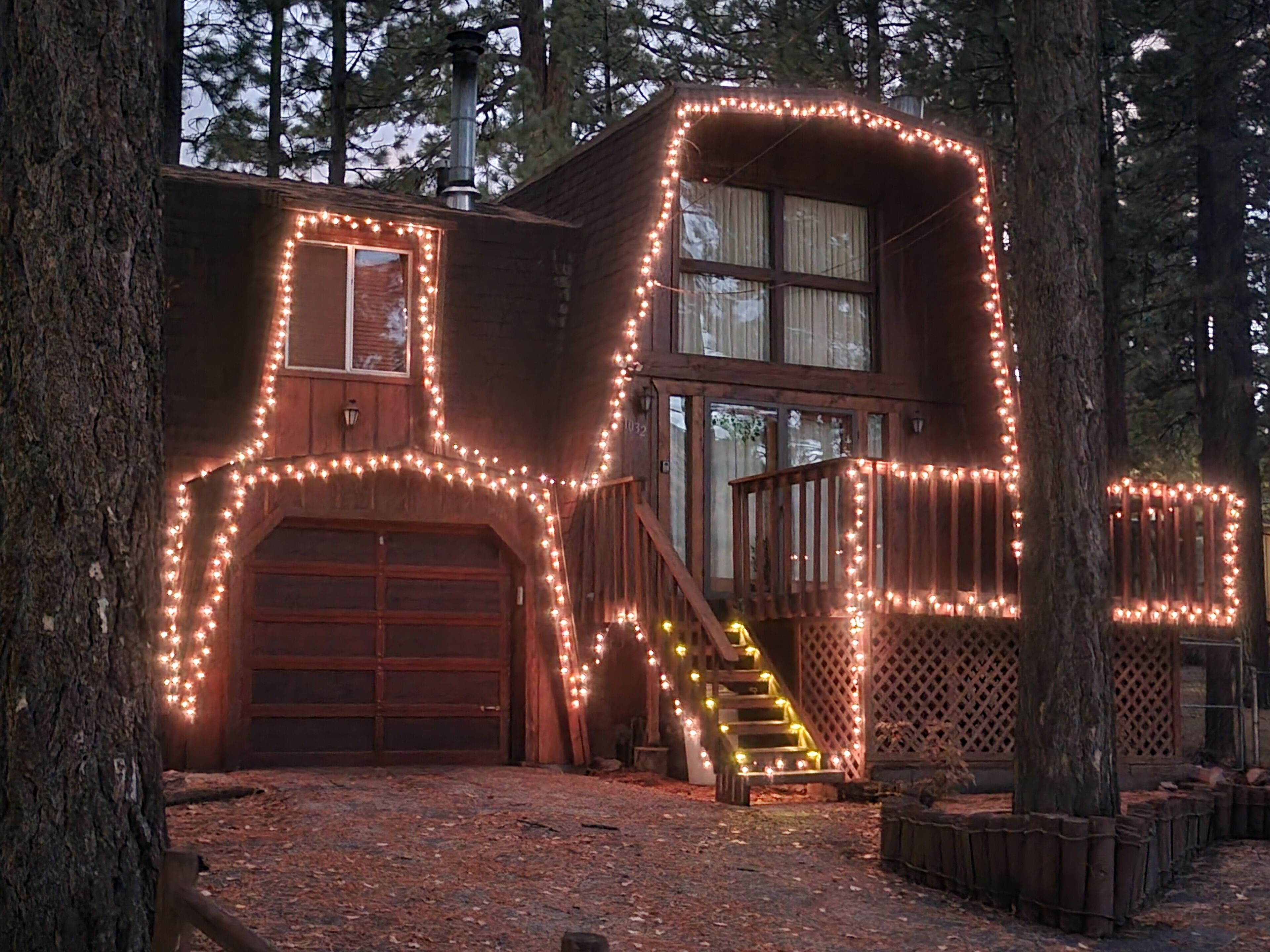 A house with a garage and a staircase leading to a deck, surrounded by trees.