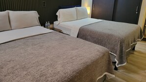 A hotel room with two beds, a dark headboard, a wooden floor, and a nightstand with a water bottle. - Double room 04 with 2 double beds, air conditioning, private bathroom (San Salvador)