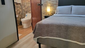 A bedroom with a bed, a wooden floor, a stone wall, a toilet, and a nightstand with a lamp. - Double room 04 with 2 double beds, air conditioning, private bathroom (San Salvador)