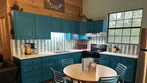 A kitchen with teal cabinets, a wooden table, and chairs. There is a red microwave, a black stove, and a window with a view of trees. - Crystal Clear Frio River - Private Waterfront House - Room for the Family (Concan)