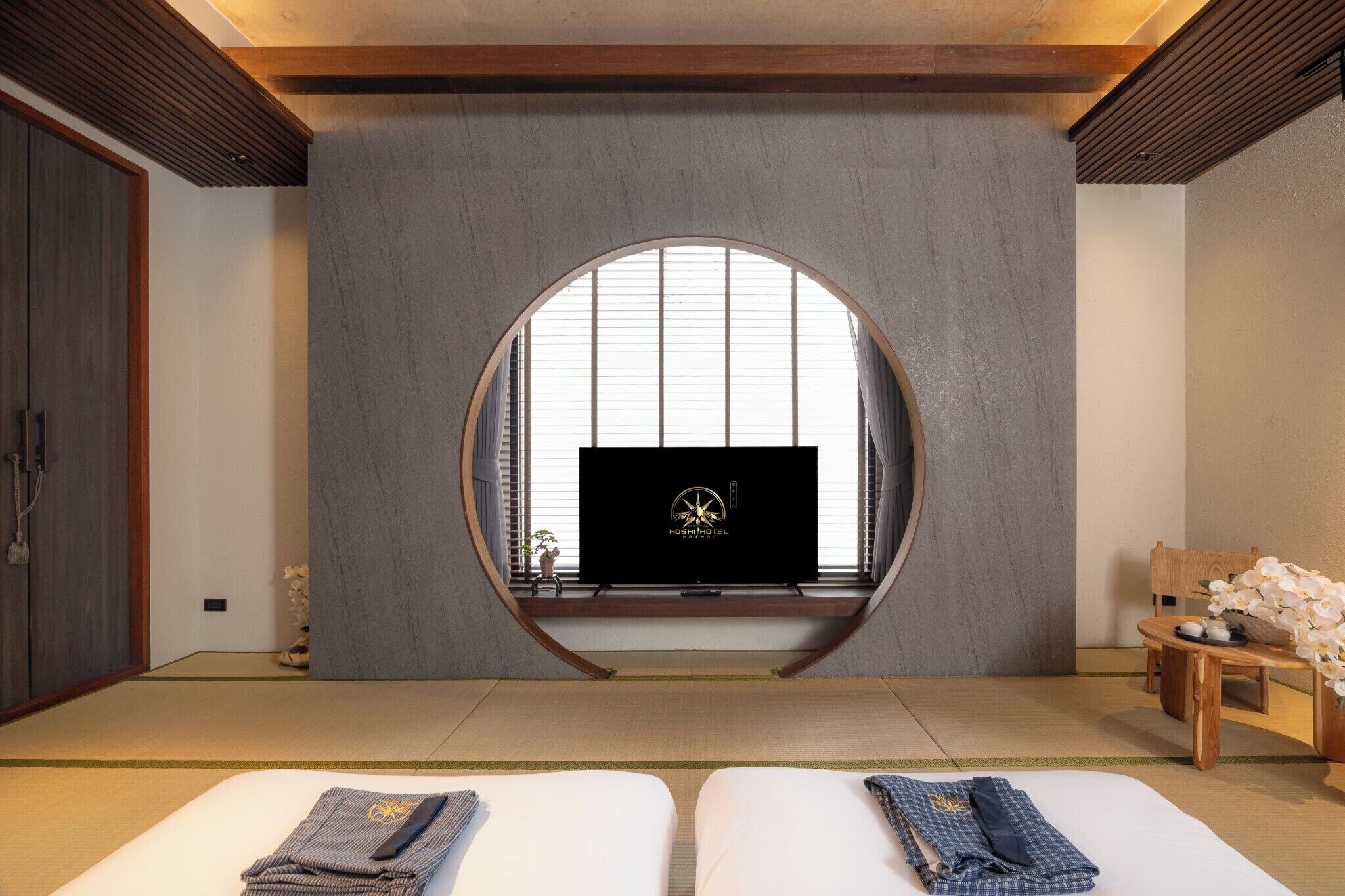 A room with tatami flooring, a television on a shelf, a wooden bench, and a bed with neatly folded clothes.
