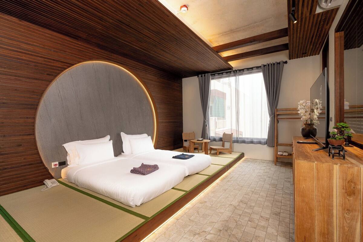 A modern hotel room with a large bed, a small desk, a chair, and a large mirror.