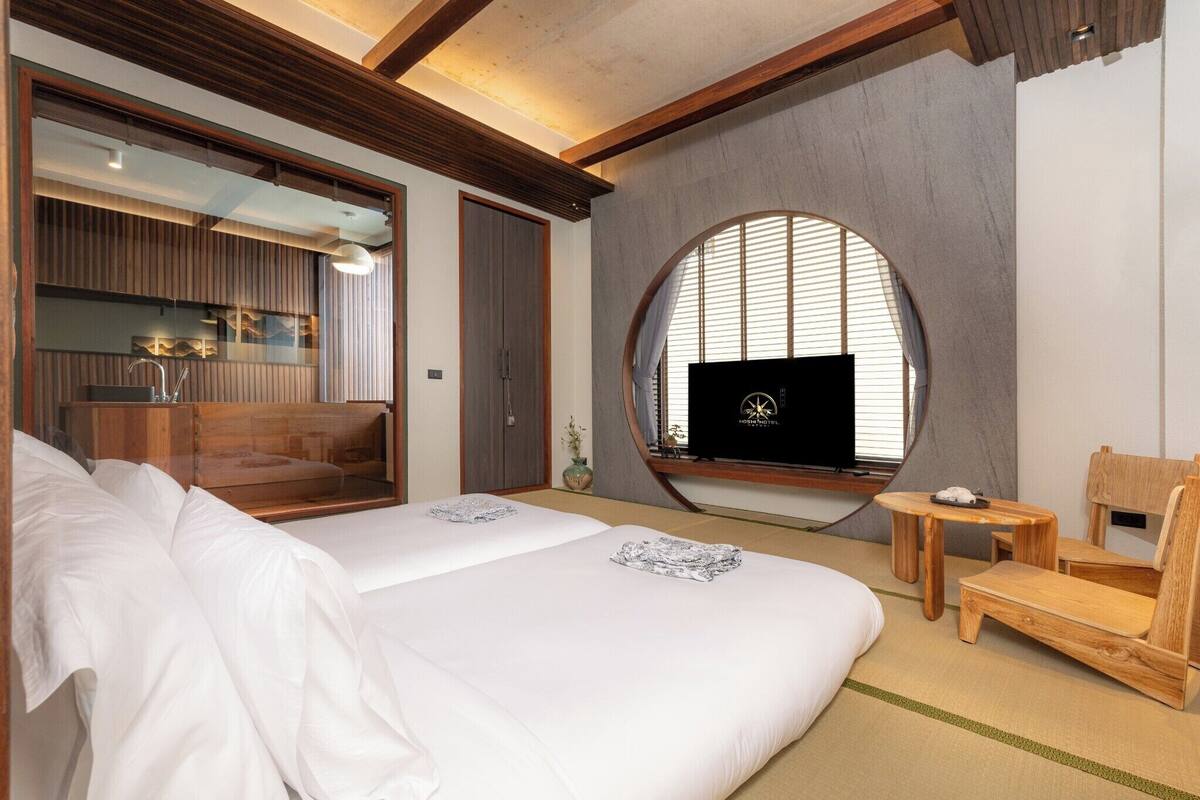 A modern hotel room with a large bed, a TV, a wooden chair, and a small table.