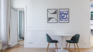 Habitació moderna amb una taula blanca i dues cadires verdes, una porta blanca i una finestra amb vistes.