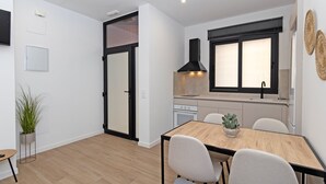 A modern kitchen with a black stove, a window with blinds, and a dining area with a wooden table and chairs.