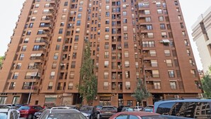 A tall brick apartment building with multiple balconies and air conditioning units.