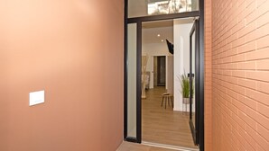A hallway with a glass door leading to a room with a bed, a small table, and a potted plant.
