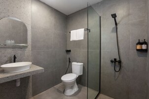 Un baño moderno con ducha separada por vidrio, un inodoro blanco y un lavamanos con espejo.