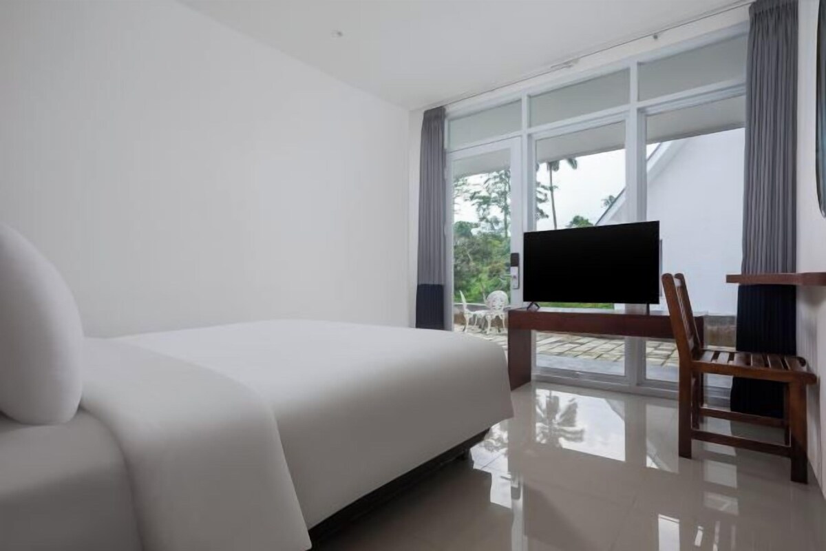 Een hotelkamer met een bed, een televisie, een houten stoel en grote ramen.