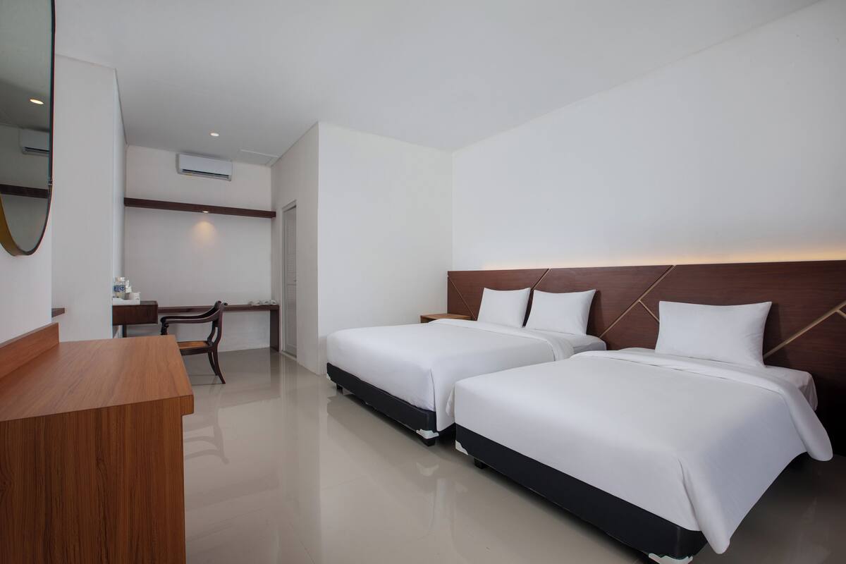Una habitación de hotel con dos camas, un escritorio de madera, una silla y un espejo.