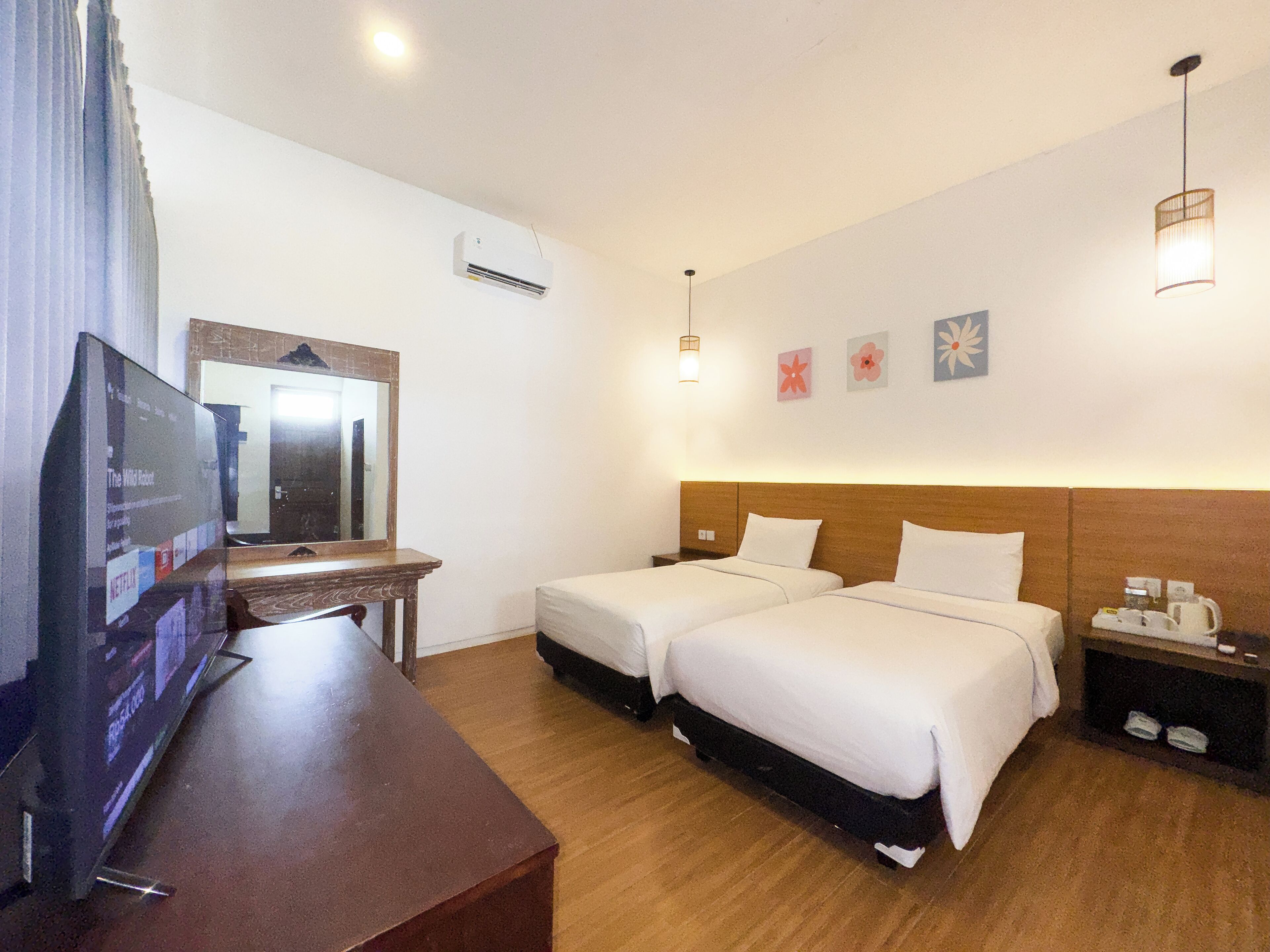 A hotel room with two beds, a TV, a desk, and a mirror.