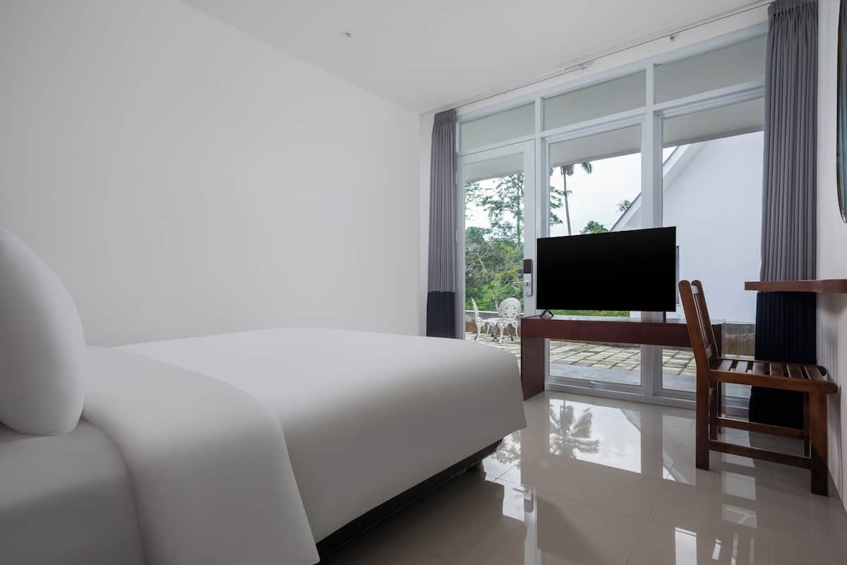 Habitación de hotel con una cama grande, televisión y vistas al exterior a través de un ventanal.