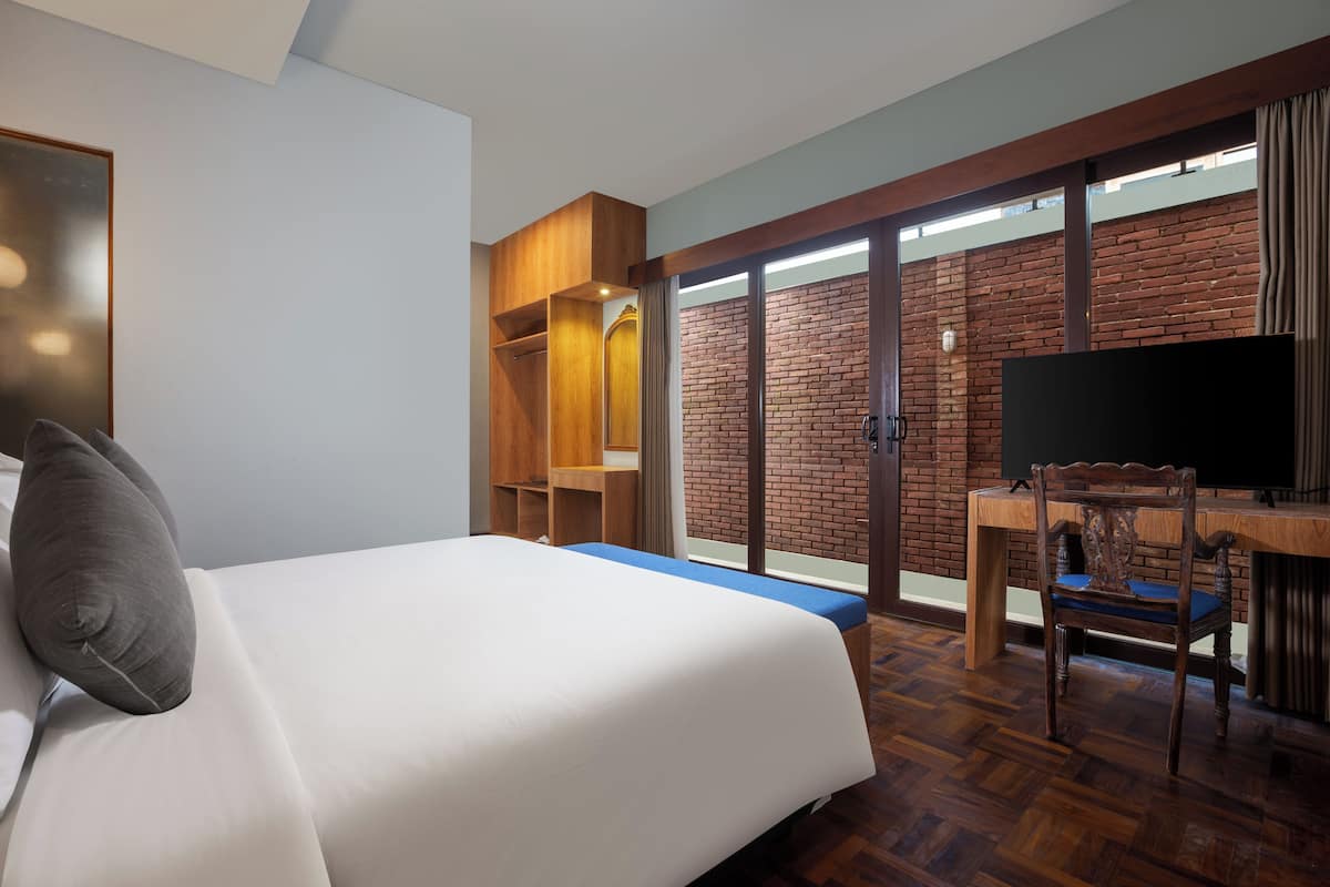Una habitación de hotel con una cama grande, un escritorio de madera, un televisor y una pared de ladrillo.