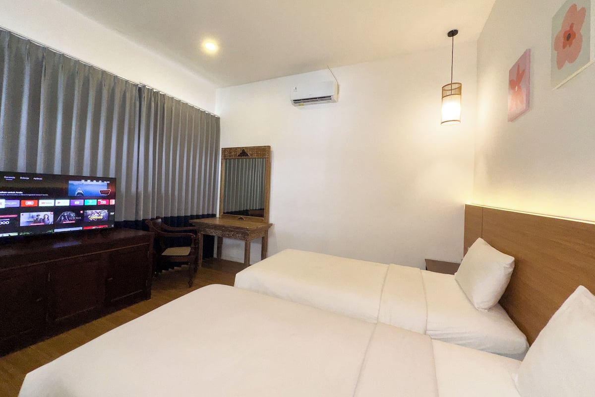 Una habitación de hotel con dos camas, un escritorio, televisor y espejo.