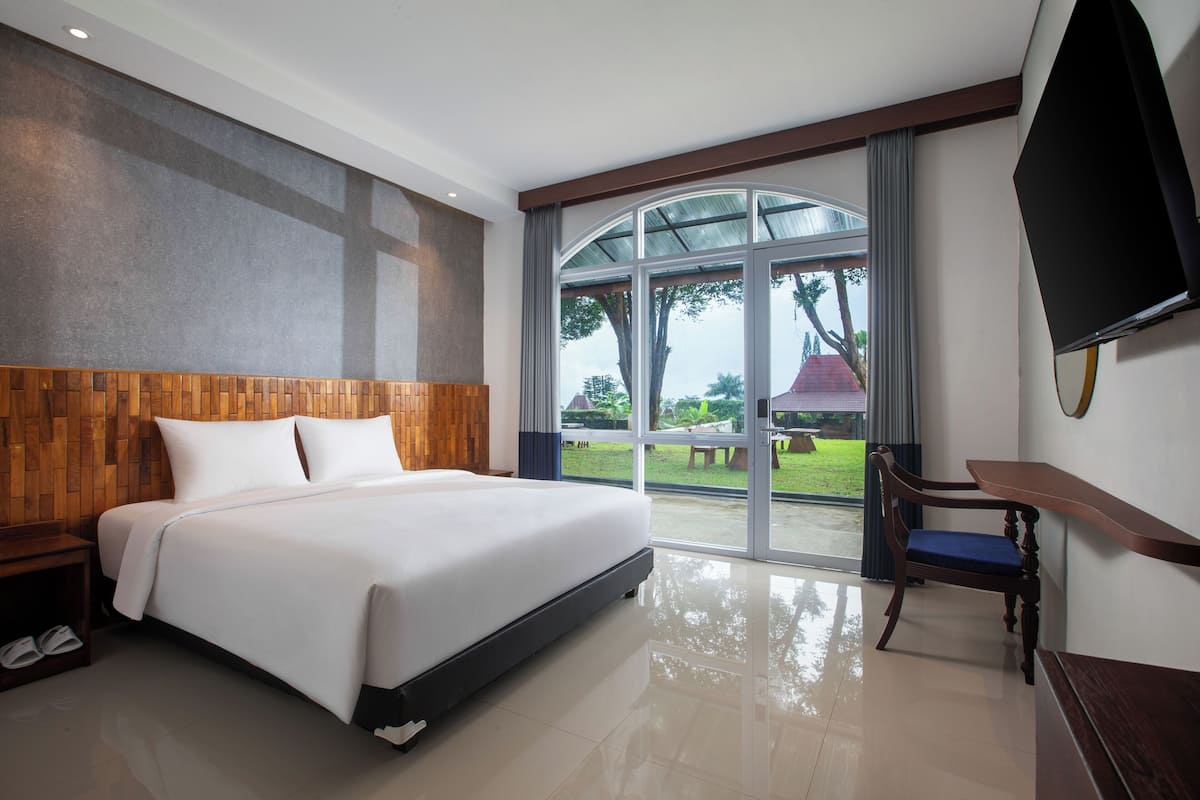 Habitación de hotel con una cama grande, cabecera de madera, televisor de pantalla plana, escritorio con silla y una ventana amplia con vistas al exterior.