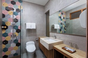 Un baño moderno con ducha de azulejos hexagonales, inodoro, lavamanos y espejo.
