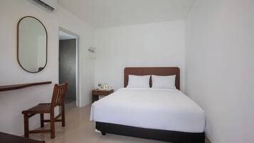 Quarto de hotel com uma cama, uma cadeira de madeira, uma mesa de cabeceira, um espelho e um ar condicionado.