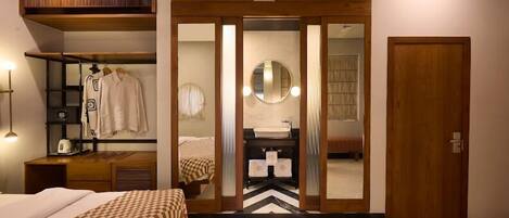 Un dormitorio con cama, armario, espejo y baño visible a través de una puerta de cristal.