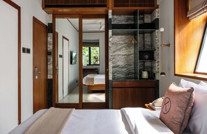 A bedroom with a bed, a wooden wardrobe, a mirror, a nightstand, and a window with curtains. - The Kin Hotel (Mumbai)