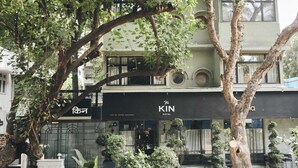 A hotel with a black awning, outdoor seating, and potted plants. - The Kin Hotel (Mumbai)