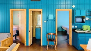 A compact, brightly colored room with wooden furniture, a small kitchen area with a microwave, and a single chair. - Beautiful Secluded Cabin in the Woods - Second Wind Ranch (Leakey)
