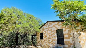 A rustic stone building with a window, surrounded by trees and a dirt path. - Beautiful Secluded Cabin in the Woods - Second Wind Ranch (Leakey)