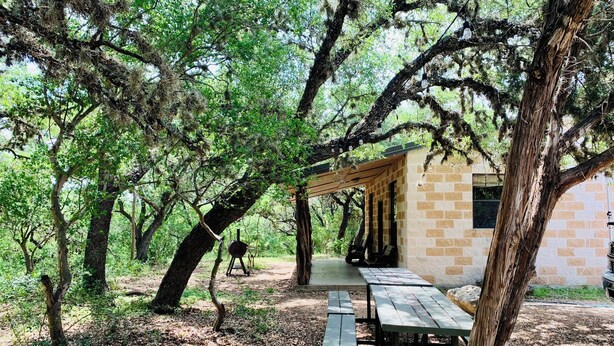A rustic outdoor pavilion with picnic tables and a brick building in a wooded area. - Beautiful Secluded Cabin in the Woods - Second Wind Ranch (Leakey)