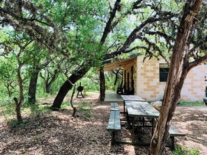 Un pavillon rustique en plein air, doté de tables de pique-nique, et un bâtiment en briques situé dans une zone boisée.