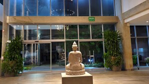 A modern building entrance with a Buddha statue in the center, large windows, and a circular light fixture above.
