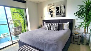 A modern bedroom with a large bed, a view of the ocean, and a balcony with a birdcage.