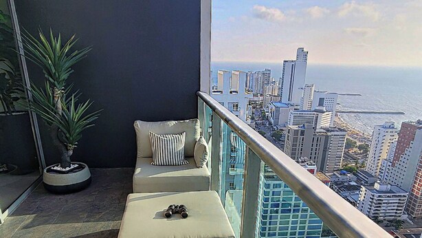 A balcony with a city view, a potted plant, and a wicker chair.