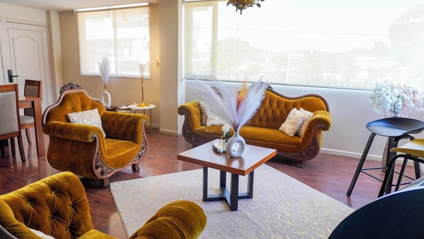 A living room with two mustard-colored sofas, a wooden coffee table, and a white vase with feathers.