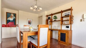 A dining area with a wooden table and chairs, a chandelier, and a bookshelf with various items.