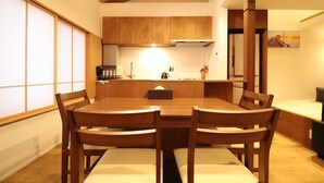 Un coin repas avec une table et des chaises en bois, une cuisine à l’arrière-plan et une porte coulissante sur la gauche.
