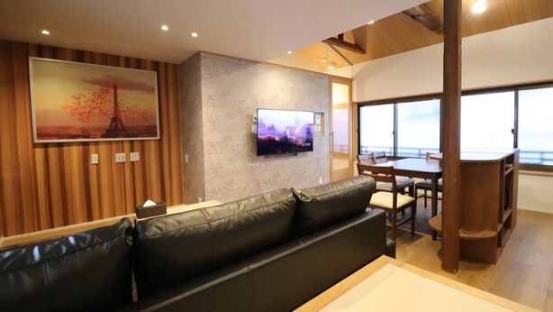 Un salon moderne avec un canapé en cuir, un téléviseur à écran plat fixé à un mur texturé et un coin repas comprenant une table et des chaises en bois.