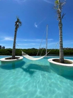 A pool area with two palm trees and a hammock. - Spacious 3BR Marina Condo with Pool (Mazatlan)