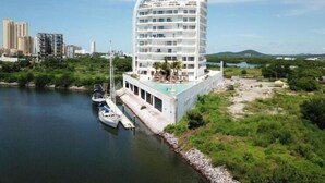 Ein modernes Hotel mit geschwungener Fassade, einem Dachpool und einer Marina mit Booten.